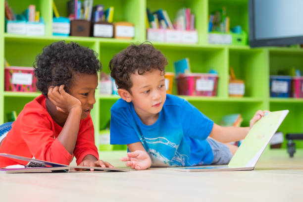 два мальчика ребенок лег на пол и чтение сказки книги в дошкольной библиотеке, детский сад школьное образование концепции - child at library стоковые фото и изображения