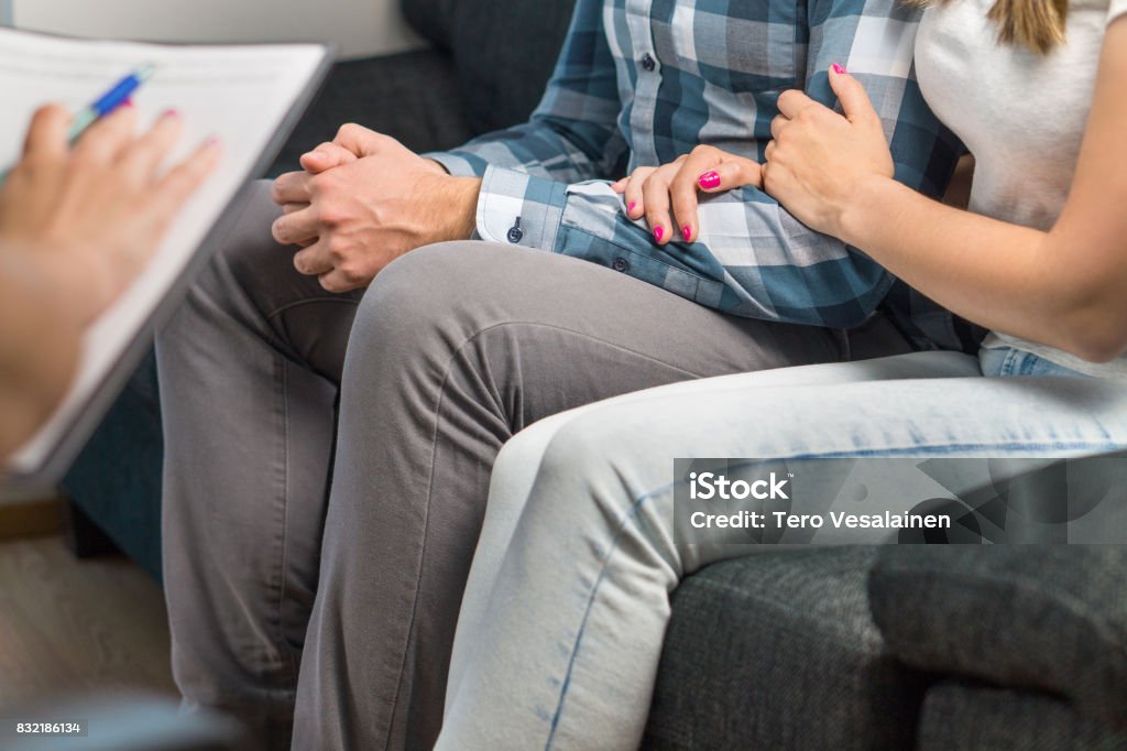 Couples therapy or marriage counseling. Woman hugging man's hand on couch during a psychotherapy session. Psychologist, counselor, therapist, psychiatrist or relationship consultant giving advice. Couples therapy or marriage counseling. Woman hugging man's hand on couch during a psychotherapy session. Couple - Relationship Stock Photo