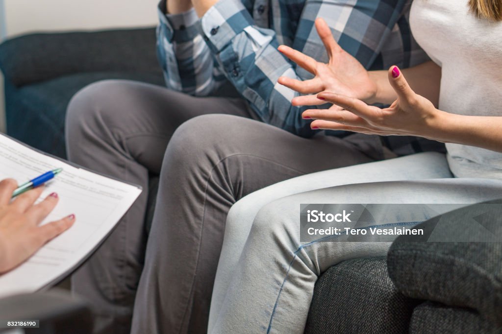 Couple having fight in therapy or marriage counseling. Man and woman sitting on couch. Wife waving hands. Session with psychologist, counselor, therapist, psychiatrist or relationship consultant. Couple having fight in therapy or marriage counseling. Man and woman sitting on couch. Wife waving hands. Child Custody Stock Photo