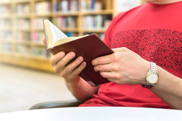 istock Young athletic man or student reading a book in public or school library in college or university. Education, studying and literature service concept. Bookshelf and bookcase in the background. 832186976