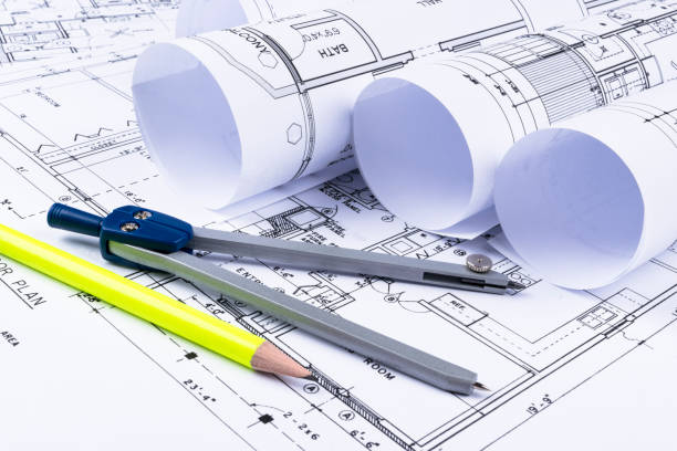 istock Architectural blueprint drawings of the modern house with computer keyboard. Architectural blueprints and blueprint rolls and a drawing instruments on the worktable. Drawing compass, plans. 832243076