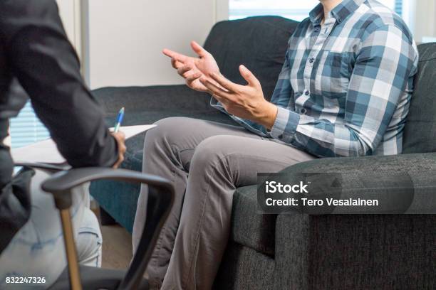 Man Talking And Waving Hands In Therapy Session With Psychiatrist Psychologist Counselor Therapist Or Life Coach Meeting With Professional Specialist With A Notepad Male Patient Sitting On Couch Stock Photo - Download Image Now