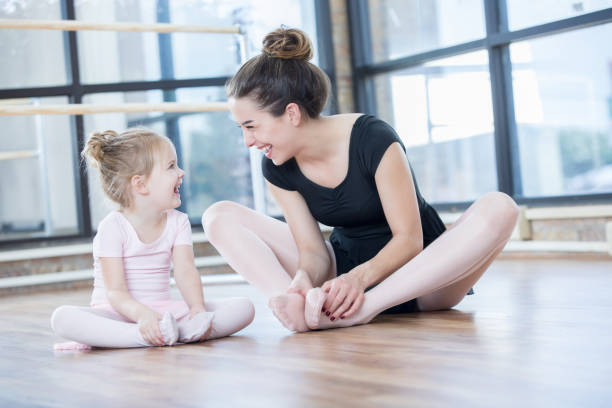 Young ballet instructor laughs with preschool age student A young ballet instructor sits on the floor with her adorable young preschool age student as they look at each other and laugh while stretching. dance studio instructor stock pictures, royalty-free photos & images