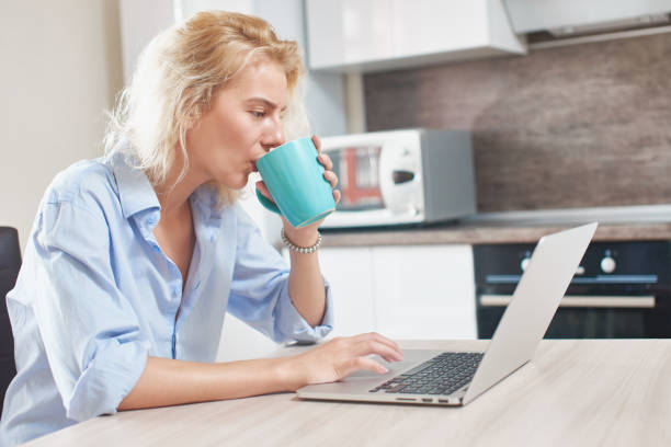 istock Young girl sitting on the kitchen table with laptop and Cup 832515006