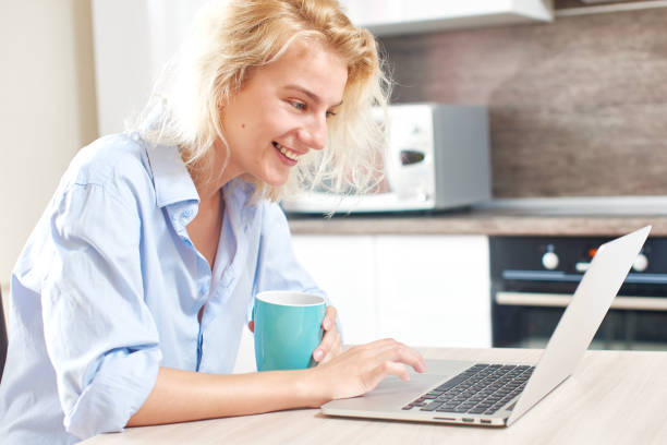 istock Young girl sitting on the kitchen table with laptop and Cup 832515214