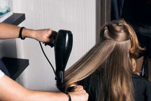 Young woman doing hair styling in the salon. Young woman doing hair styling in the salon. The hairdresser combs her hair. blow drying stock pictures, royalty-free photos & images