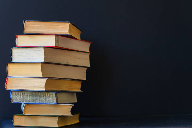 Close-up of a stack of thick books in hard multicolored bindings on a black background. Place for text, the concept of starting school, back to school, education