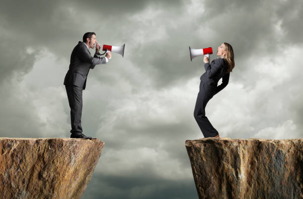 Businessman And Businesswoman Standing On Opposite Cliffs Shout At Each Other A businessman and a businesswoman standing on opposite cliffs shout at each other through their megaphones. communication problems stock pictures, royalty-free photos & images