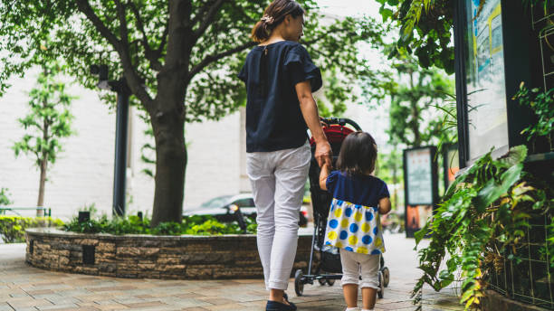 都市公園を歩いて母と赤ちゃんの女の子の後姿 - ベビーカー ストックフォトと画像