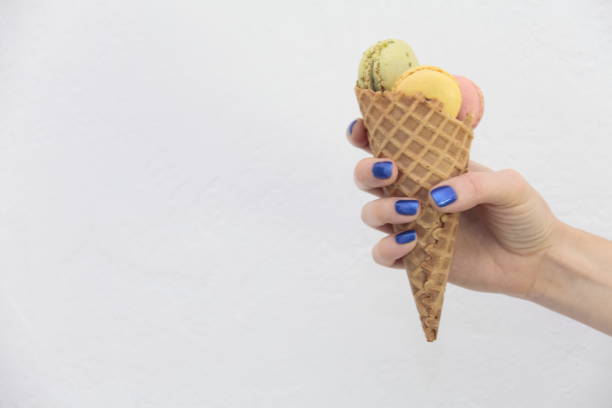 istock Female hand holding ice cream cone with macaroons. 832682696