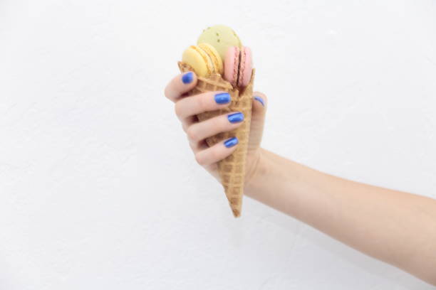 istock Female hand holding ice cream cone with macaroons. 832683124