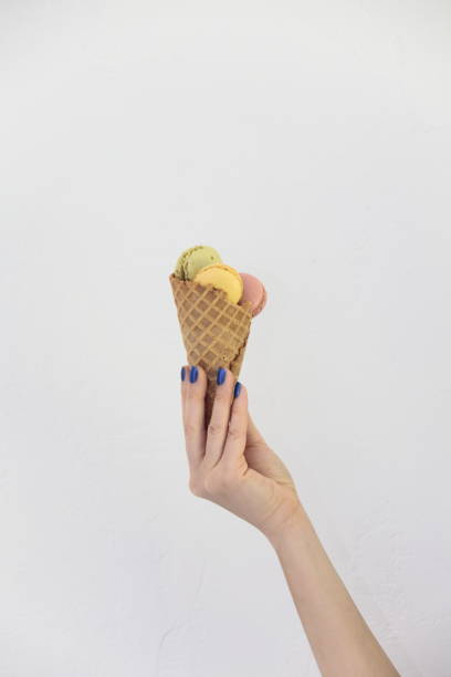 istock Female hand holding ice cream cone with macaroons. 832689644