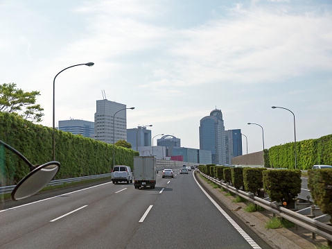 Driving by eco friendly highway in Tokyo, tall green Overgrown noise barriers with grass on roadsides, city ahead, Japan