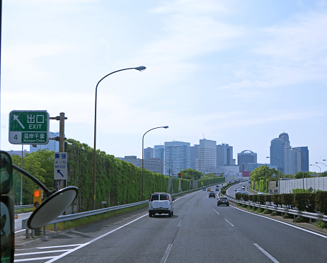 Driving by eco friendly highway in Tokyo, tall green Overgrown noise barriers with grass on roadsides, city ahead, Japan