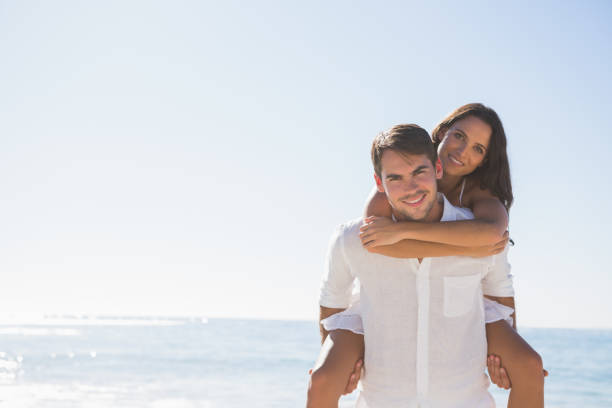 istock Smiling man giving girlfriend a piggy back looking at camera 832968456
