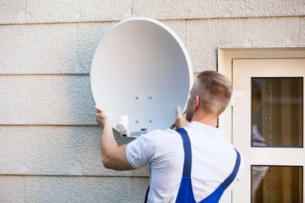 Young Male Technician Installing TV Satellite Dish To Wall