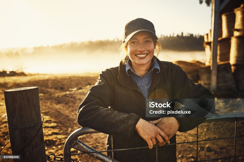 Living with nature right on my doorstep Portrait of a young woman leaning against a gate on a farm Farmer Stock Photo