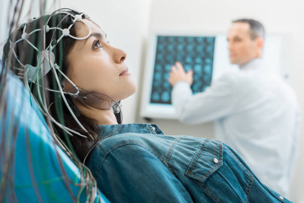 Charming young woman undergoing electroencephalography Vital procedure. Beautiful dark-haired woman lying on an examination table and undergoing electroencephalography while her doctor examining CT results animal internal organ stock pictures, royalty-free photos & images