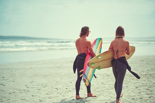 Shot of a young couple walking on the beach with their surfboards
