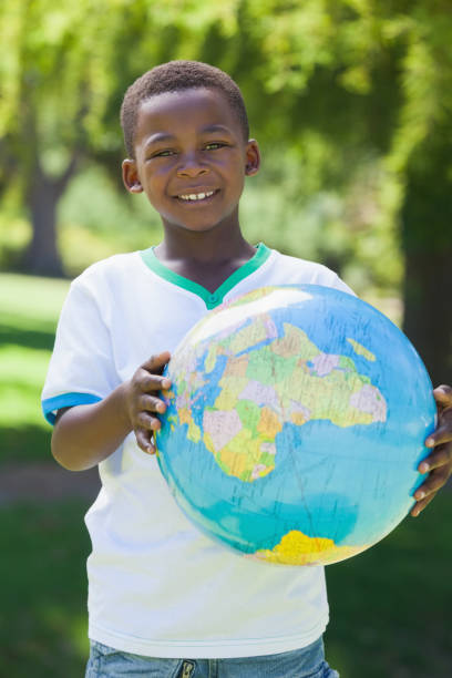 istock Little boy smiling at camera holding globe in the park 833042736