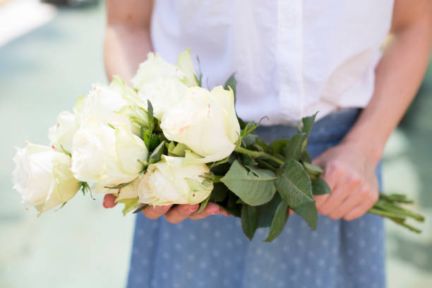 Close up of woman holding bouquet of white roses, midsection.