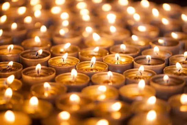 Bright warm glow from candle flames. Many beautiful lit tealight candles glowing with a golden yellow light.