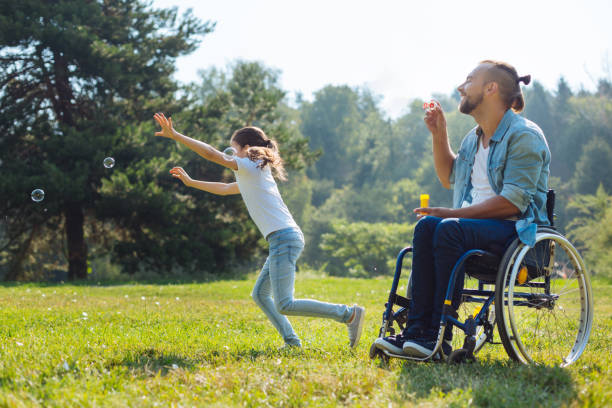 gai désactivé père et fille jouant avec des bulles de savon - sports en fauteuil roulant photos et images de collection
