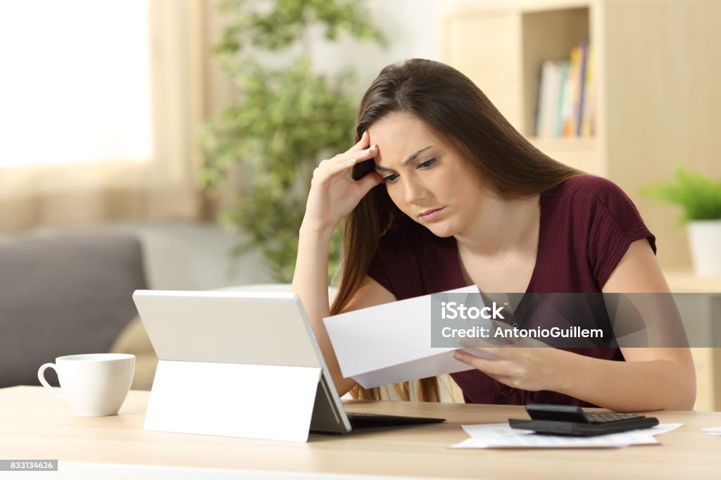 Worried woman calculating accountancy reading a letter Worried woman calculating accountancy reading a letter sitting in a desk at home Financial Bill Stock Photo