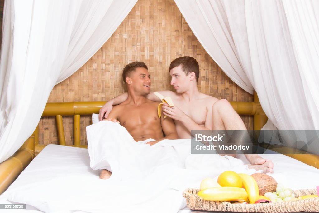 Romance and love. Holidays in the tropics. Happy couple. Attractive guys. Honeymoon. Gay couple. Two sexy men. Bed - Furniture Stock Photo