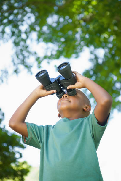 Little boy looking up through binoculars in the park on a sunny day