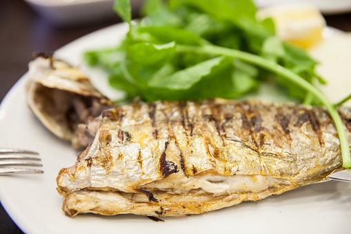 Delicious baked mackerel fillets with greens, garlic and lemon on wooden board. Wooden background. Top view.