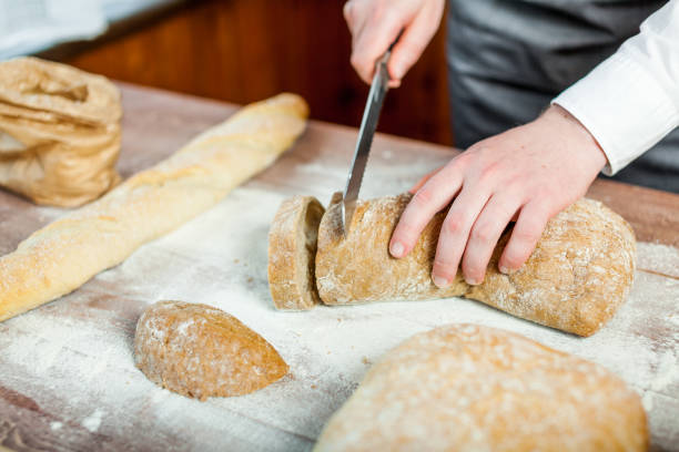 istock Male hands cutting fresh bread on the wooden table, selective focus 833169736
