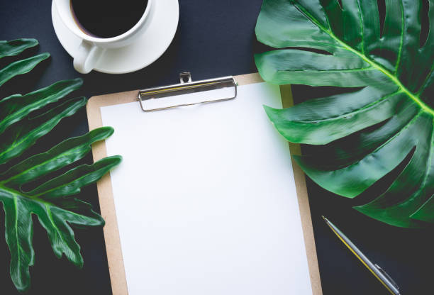 istock Blank notepaper with tropical leaves and accessories on black table. 833204456