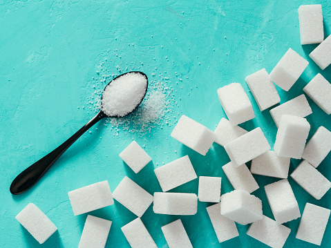 background of sugar cubes and sugar in spoon. White sugar on turquoise background. Sugar with copy space. Top view or flat lay