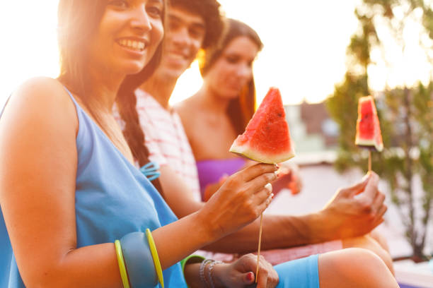 istock Girls holding watermelon slices on sticks on rooftop 833238046