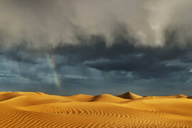 Sahara sand dunes with stormy, cloudy sky and rainbow at Erg Lihoudi. stock photo