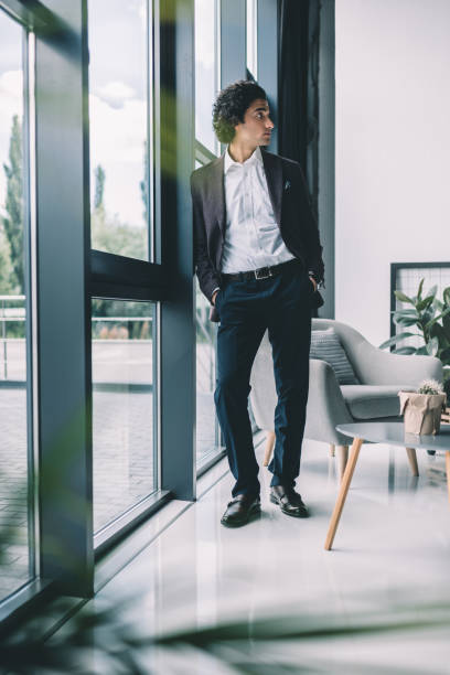 istock thoughtful businessman with hands in pockets standing at window in office 833266246