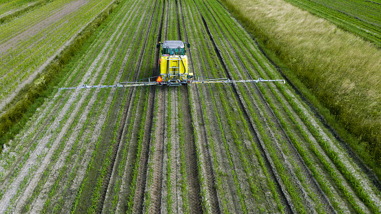 Aerial view of crop sprayer spraying pesticides on crops in field.