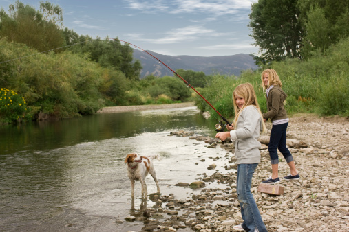 Sisters fishing by river with family dog