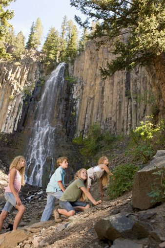 Brother and sisters climbing up rocks with view of waterfall in the background