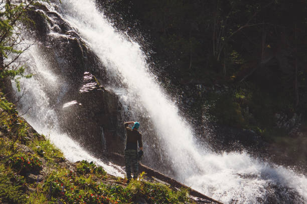 Hikers man backpacker looking at a waterfall in the forest. Hiking. Hikers man backpacker looking at a waterfall in the forest. Military exercises in the wild of Siberia. Soldiers in camouflage sneaking through the mountain river in the Caucasus spetsnaz stock pictures, royalty-free photos & images