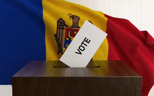 Moldovan presidential and legislative elections concept. A vote envelope is entering into a ballot box. Ballot box is in front of a waving Moldovan flag and it is made of wood. Horizontal composition with copy space. Great use for referendum and elections related concepts.