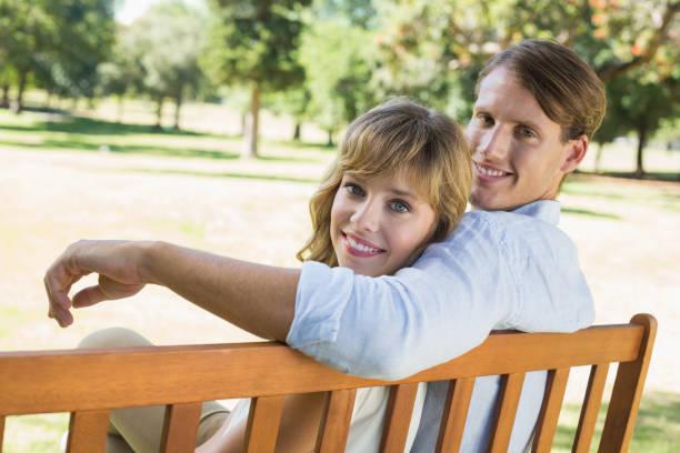 istock Couple relaxing on park bench together smiling at camera 833306438