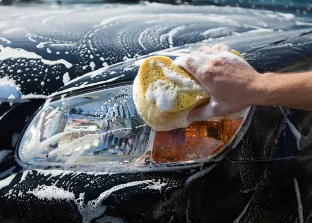 Man washing a soapy  car with a yellow sponge.