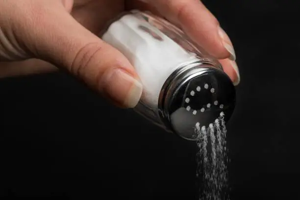 Female hand pouring salt from salt shaker on black background