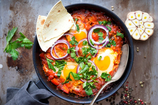 Shakshuka with pita bread Shakshuka with pita bread in a pan. Middle eastern traditional dish. Fried eggs with tomatoes, bell pepper, vegetables and herbs. Shakshouka on a table. Top view. Sunny side up eggs. From above omelet rustic food food and drink stock pictures, royalty-free photos & images