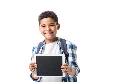 cute african american boy holding digital tablet and smiling at camera isolated on white