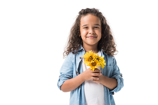 happy african american girl holding yellow flowers and smiling at camera isolated on white