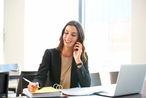 Shot of a young businesswoman sitting at office desk in front of laptop and making call while considering the possibilities with her client.