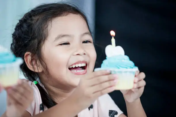 Photo of Cute asian child girl smiling and having fun to blow her birthday cupcake in party